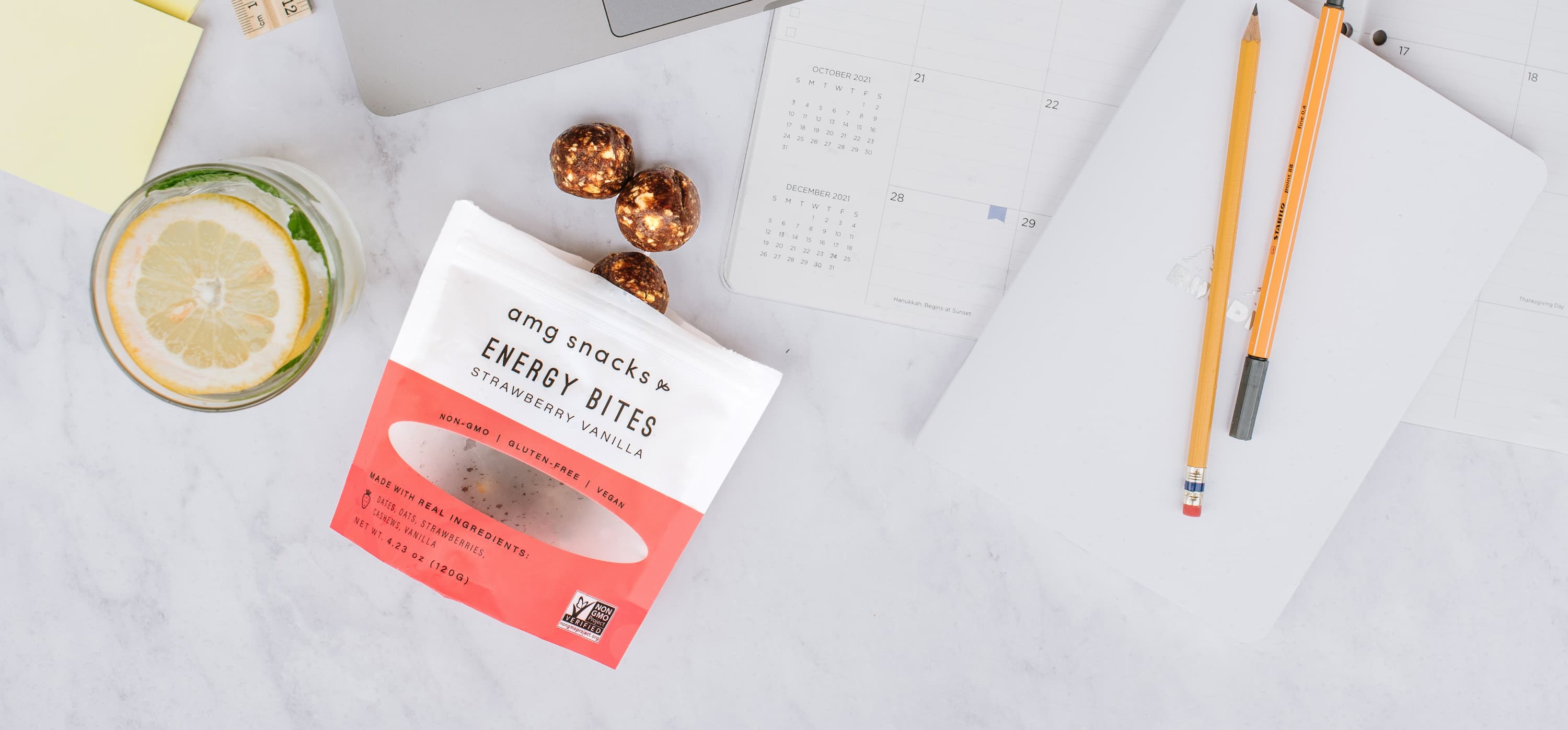 Energy Bites on marble desk with papers, pencils, lemon water.