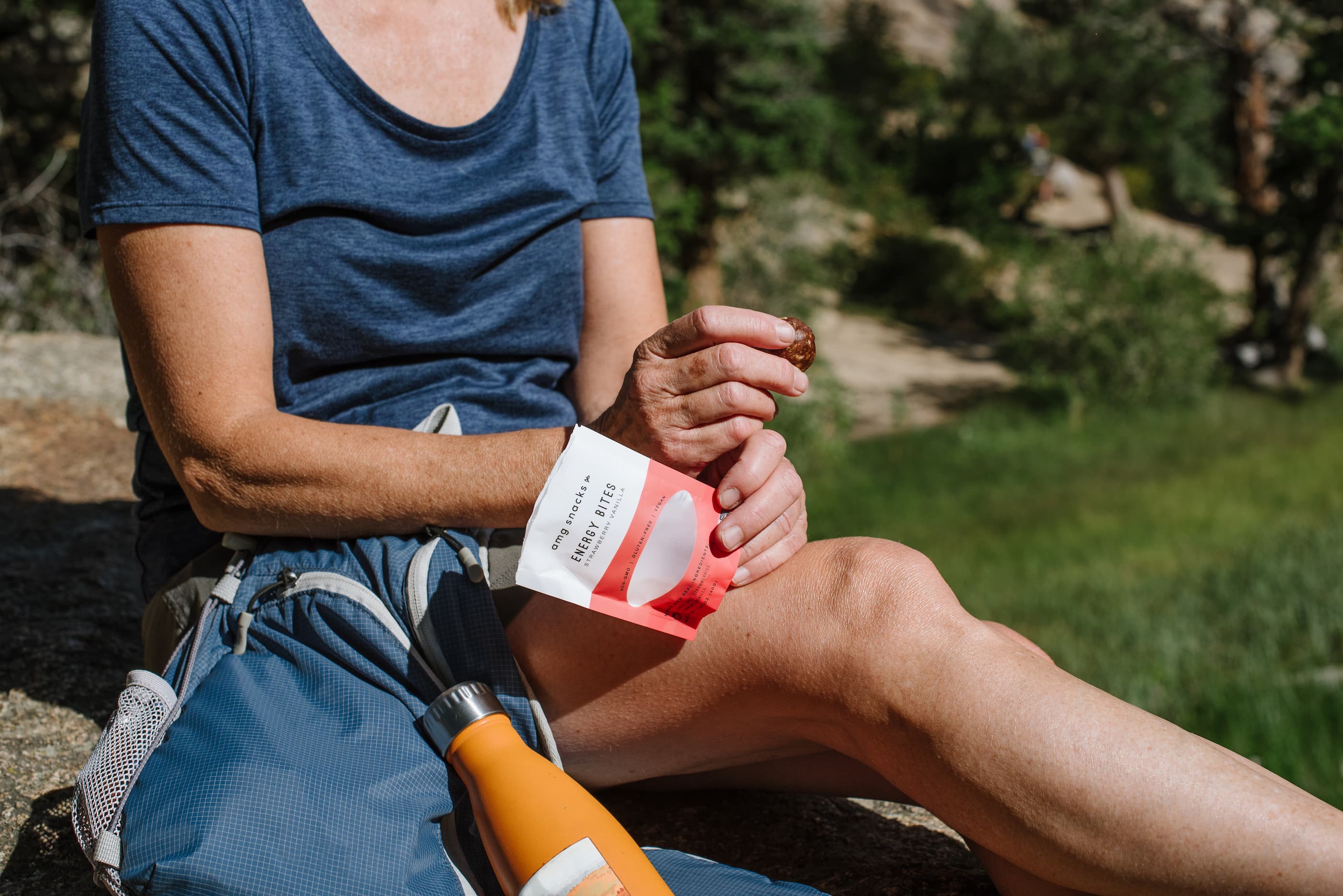 Person outdoors on rock, eating Energy Bites from a pack.