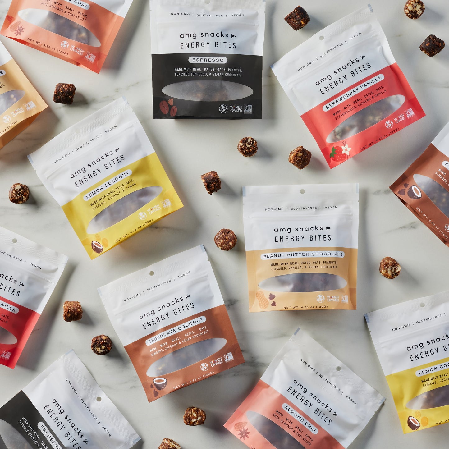 AMG Snack bags in every flavor on marble with energy bites scattered.